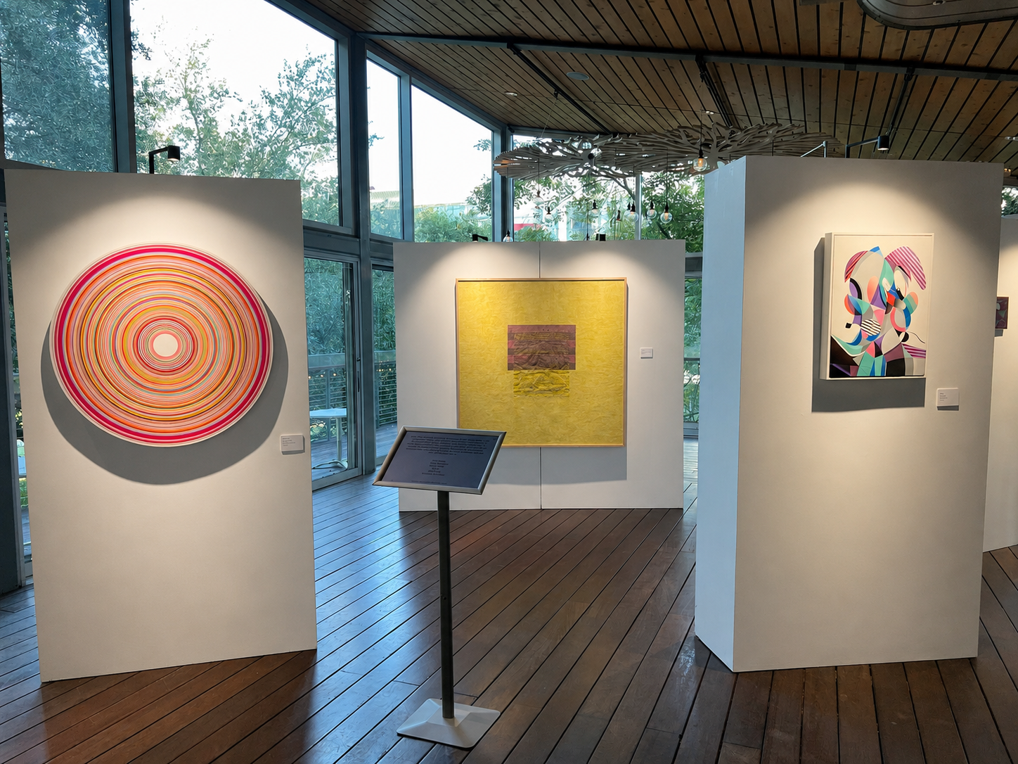 Three illuminated freestanding gallery walls displaying colorful artwork in a bright room.