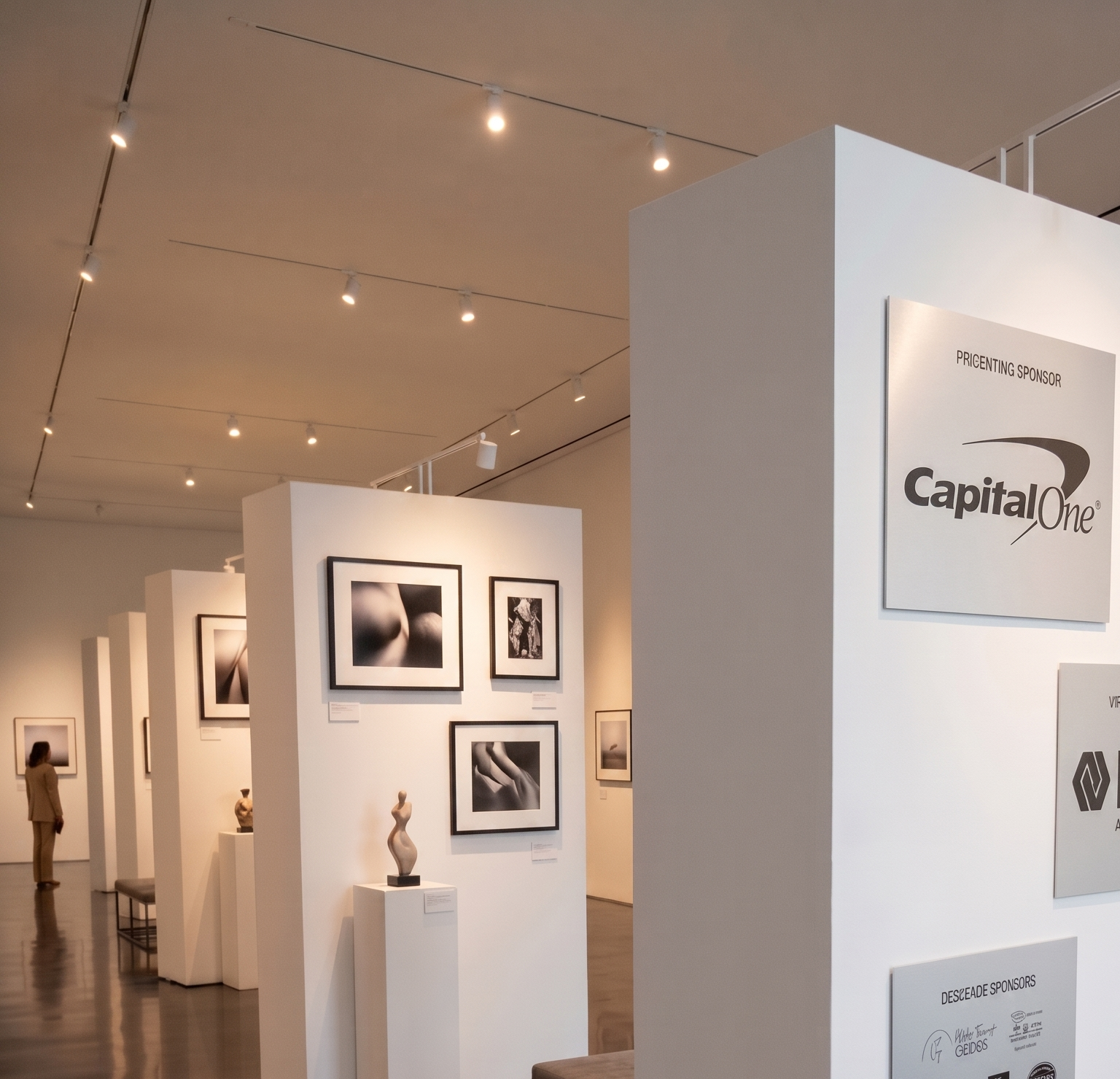 White freestanding gallery walls displaying artwork and sponsor signage in an event space.